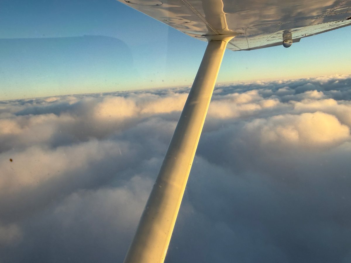Cessna wing strut above sunset-lit clouds